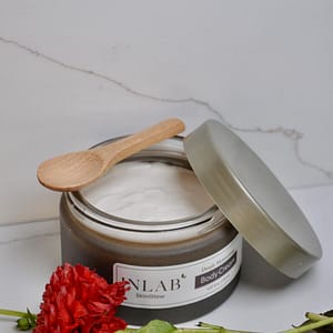 A jar of ENLAB body cream with a wooden spoon, surrounded by vibrant red flowers on a marble surface.