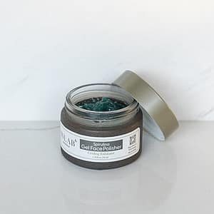 A clear glass jar of Spirulina Gel Face Polisher with a green product visible inside, partially open lid, on a white surface.