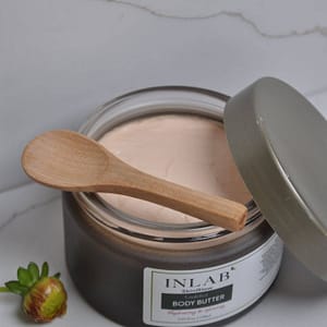 A jar of Emulsified Body Butter with a wooden spoon on top, partially open, showcasing its creamy texture against a marble background.