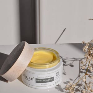 Open jar of "Deep Restore Night Cream" with rich yellow cream inside, styled with delicate dried flowers on a soft neutral background