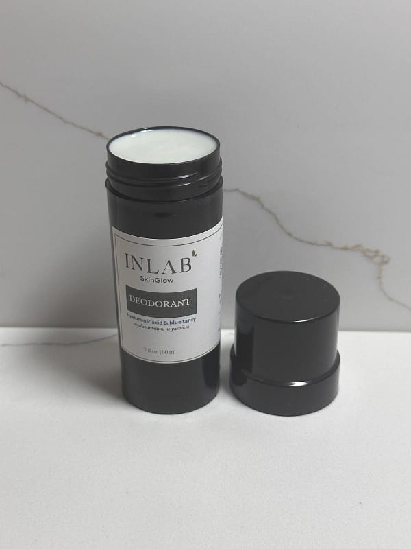 A cylindrical black container of "deodorant stick" skincare product with a white lid labeled “INLAB,” placed beside its removable cap on a plain surface.