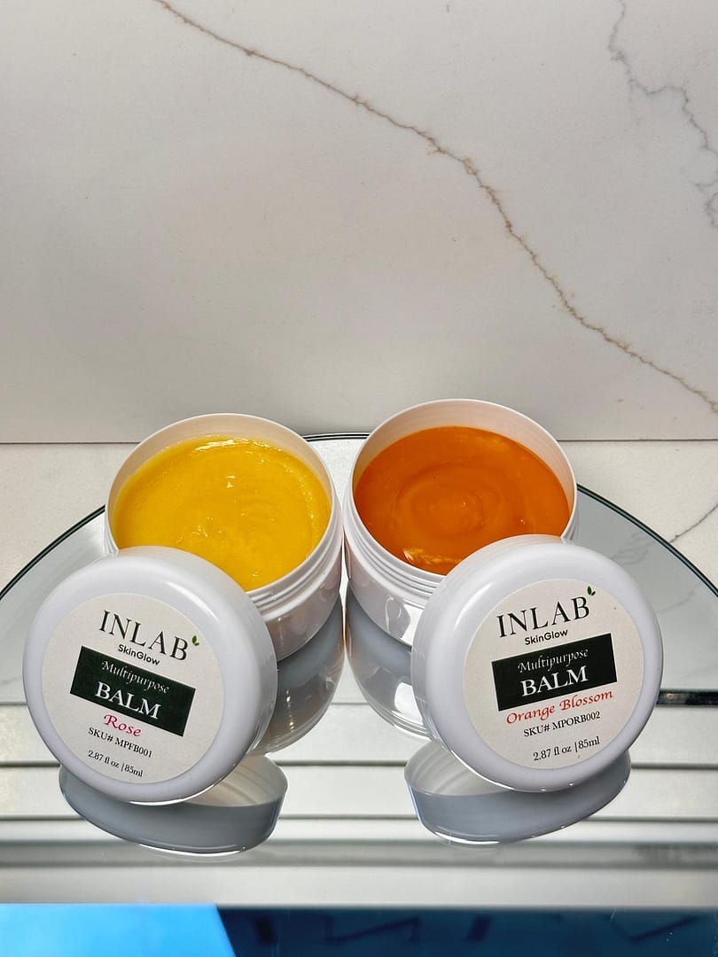 Two containers of Multi Purpose Balm one yellow and one orange, placed on a reflective surface against a minimalist background.